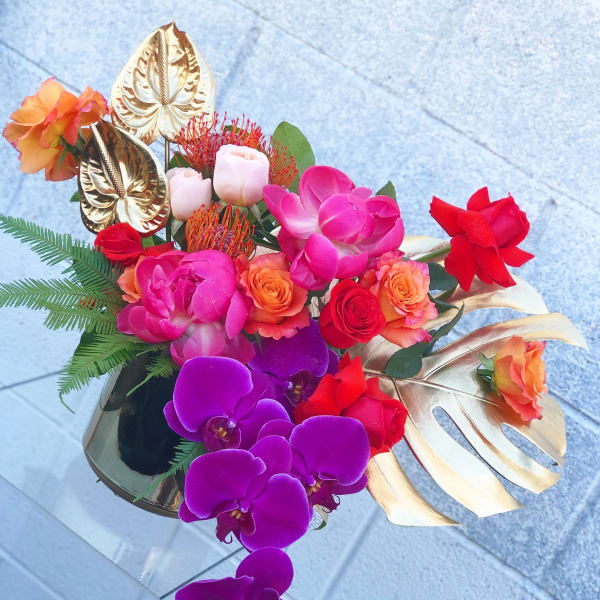 Tropical bouquet with orchids, roses, and gold leaves in a vase