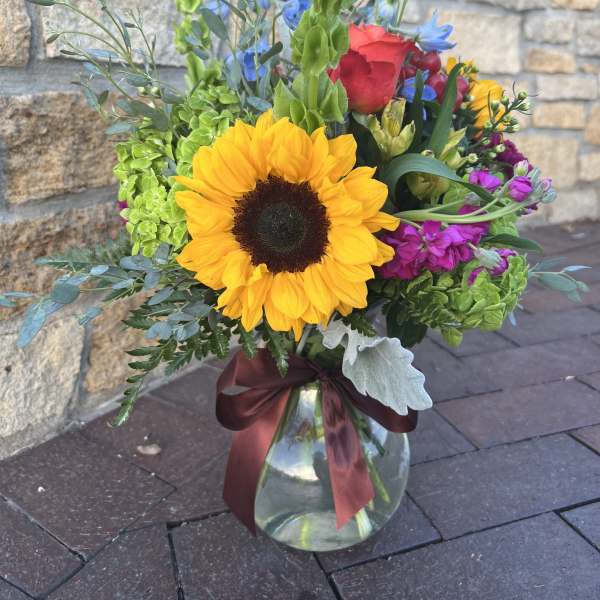 Mixed bouquet with a sunflower in a glass vase tied with a burgundy ribbon