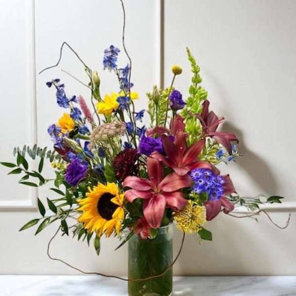 Mixed bouquet in a glass vase with sunflowers, lilies, and blue flowers