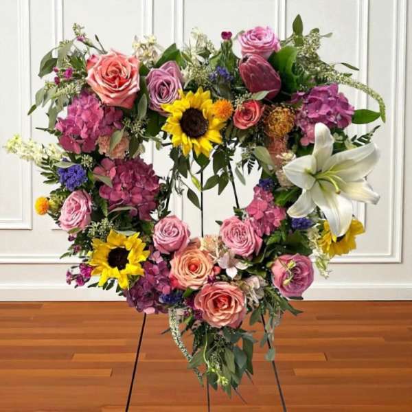Heart-shaped floral wreath with roses, sunflowers, hydrangeas, and a white lily