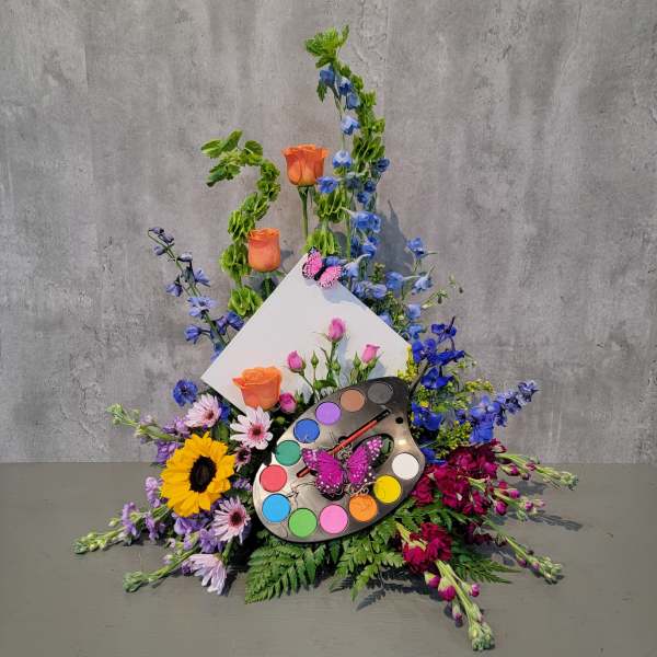 Colorful floral arrangement with roses, sunflowers, and a paint palette centerpiece