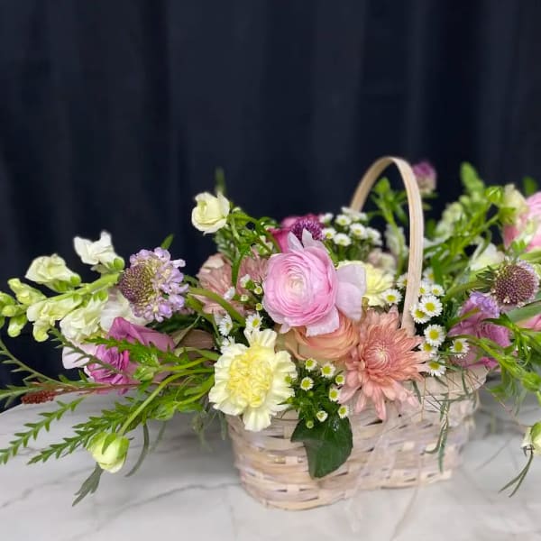 Pastel mixed flower arrangement in a wicker basket with a handle