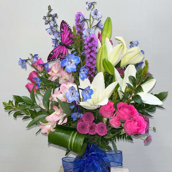 Bouquet of pink roses, white lilies, and blue flowers in a vase with a blue ribbon