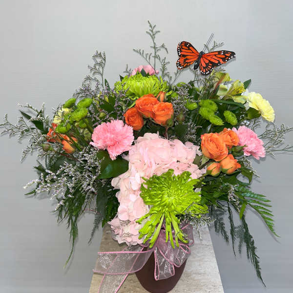 Colorful floral arrangement with roses, hydrangea, and a butterfly pick in a vase