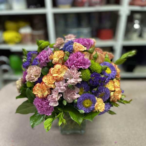 Mixed bouquet of purple, pink, yellow, and peach flowers in a glass vase