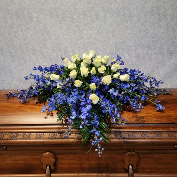 White roses and blue flowers arranged on a wooden casket