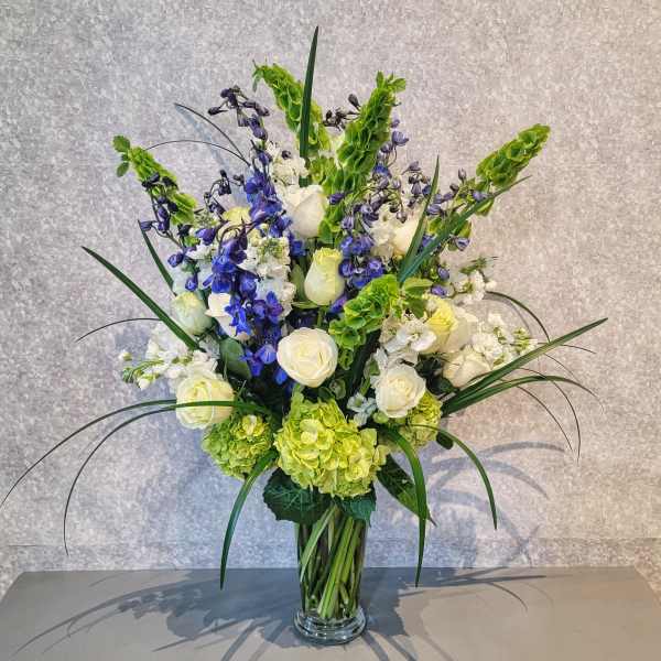 Tall bouquet of white roses, blue flowers, and green hydrangeas in a glass vase