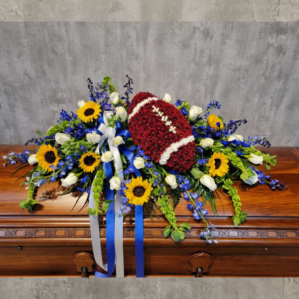 Red floral casket spray with sunflowers, white roses, and blue flowers