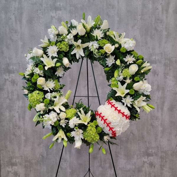White floral wreath on a stand with a baseball at the lower right