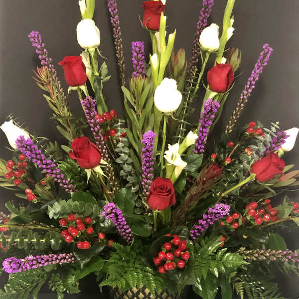 Tall arrangement of red and white roses with purple spikes in a decorative vase