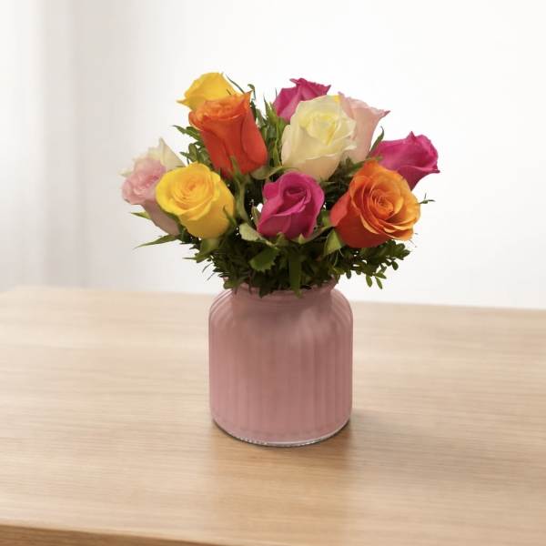 Mixed roses in a pink glass vase on a wooden table