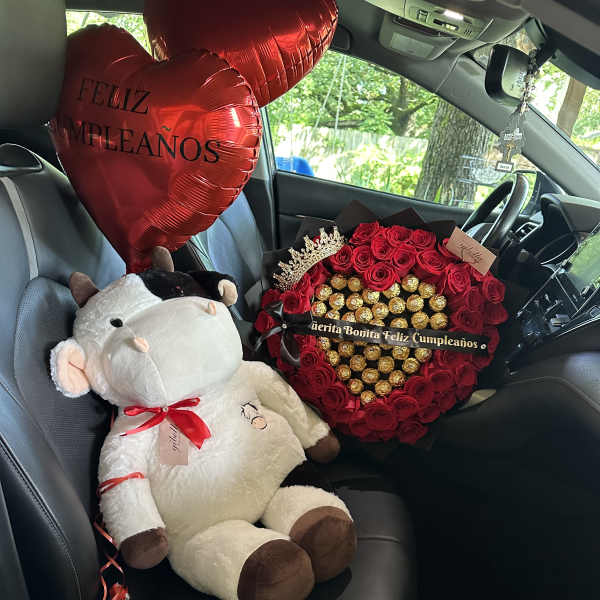 Red heart balloons, a plush cow, and a rose-and-chocolate gift arrangement in a car seat