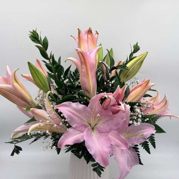 Pink lilies arranged in a white vase with greenery