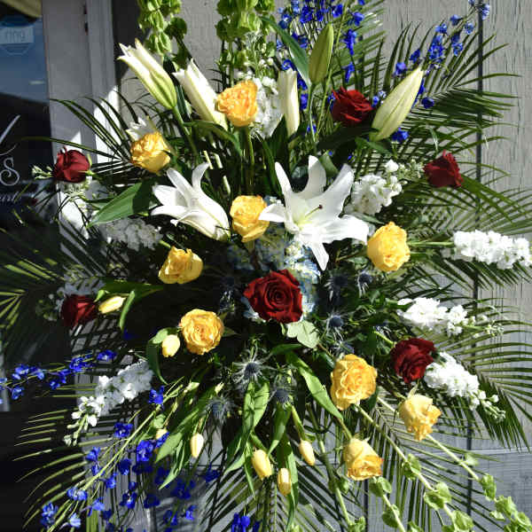 Large standing floral spray with roses, lilies, and blue flowers