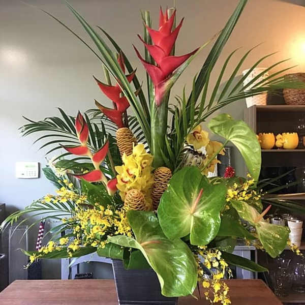 Tropical floral arrangement with red heliconia and yellow orchids in a black container