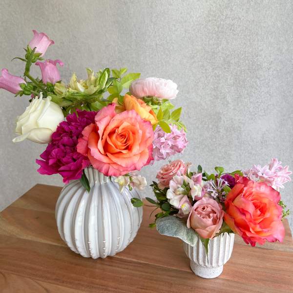 Two colorful floral arrangements in white vases on a wooden table