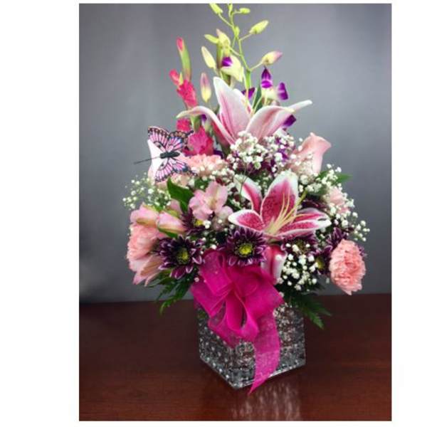 Pink and purple floral arrangement in a square glass vase with a butterfly accent