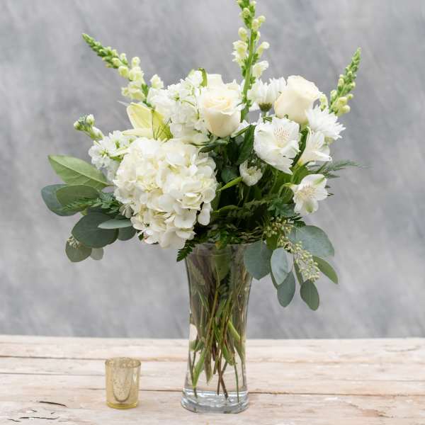 White floral bouquet in a clear glass vase with a small candle nearby