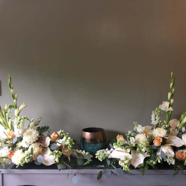 Two floral arrangements flank a small urn on a table