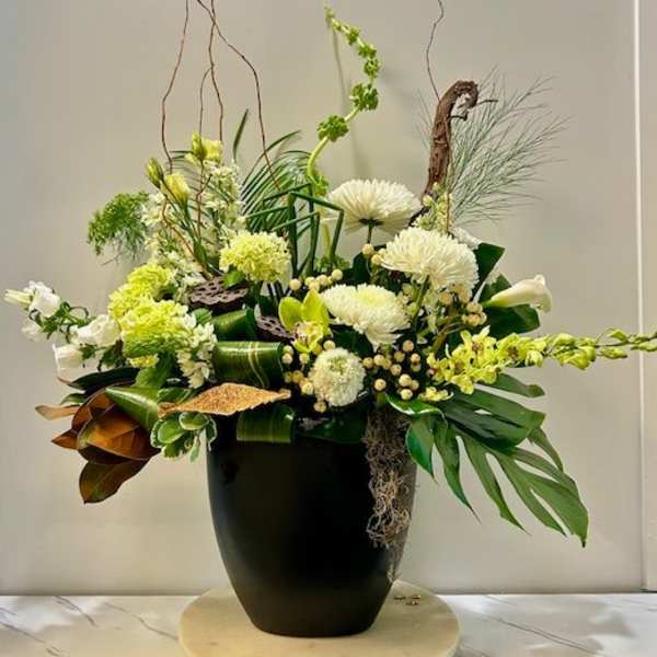 Tall floral arrangement with white and green blooms in a black vase