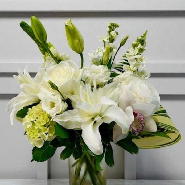 White floral arrangement in a clear glass vase with lilies and orchids