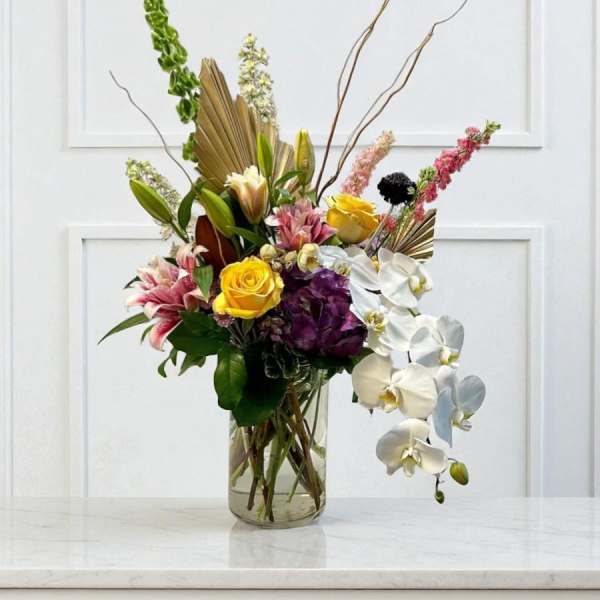 Tall mixed bouquet in a glass vase with orchids, roses, and lilies