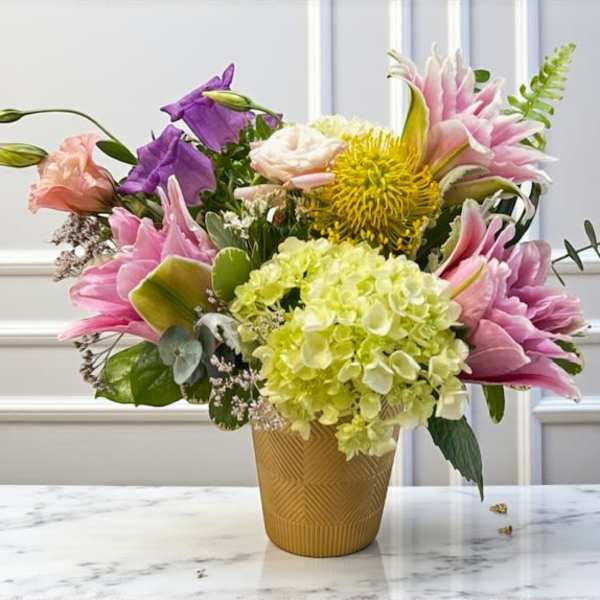 Mixed bouquet in a gold textured vase with pink, purple, and yellow blooms