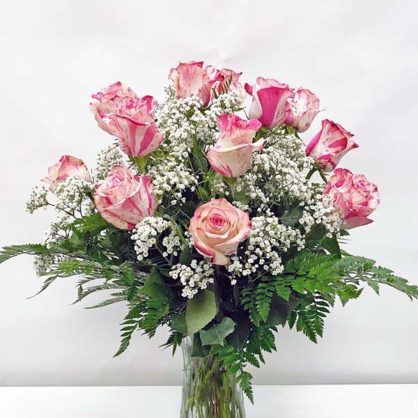Tall clear vase of pink-tipped white roses with small white filler flowers.
