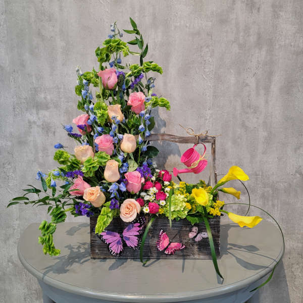 Colorful floral arrangement in a wooden box with pink roses and yellow calla lilies