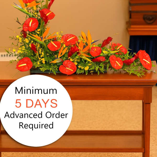 Tropical funeral spray with red and orange flowers arranged low on a wooden table