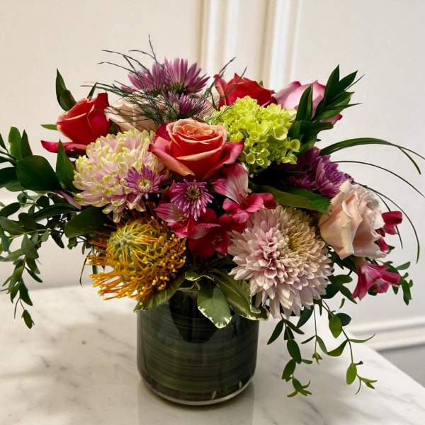Mixed bouquet of roses, chrysanthemums, and tropical blooms in a glass vase