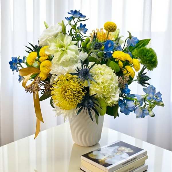 Colorful bouquet of blue, yellow, and white flowers in a white vase