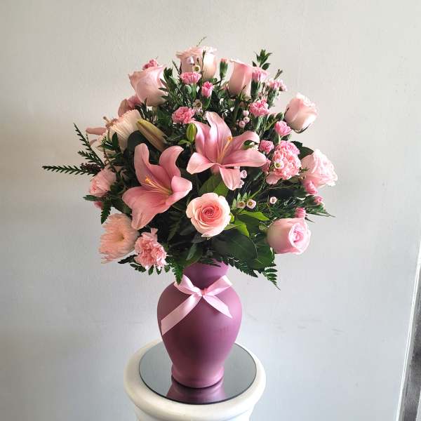 Pink floral arrangement in a purple vase with a ribbon
