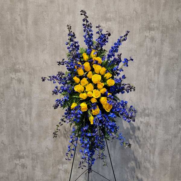 Tall standing arrangement of yellow roses and blue flowers on a black easel