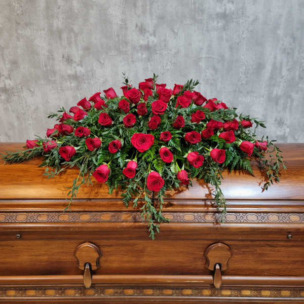 Red rose casket spray with trailing greenery on a wooden casket