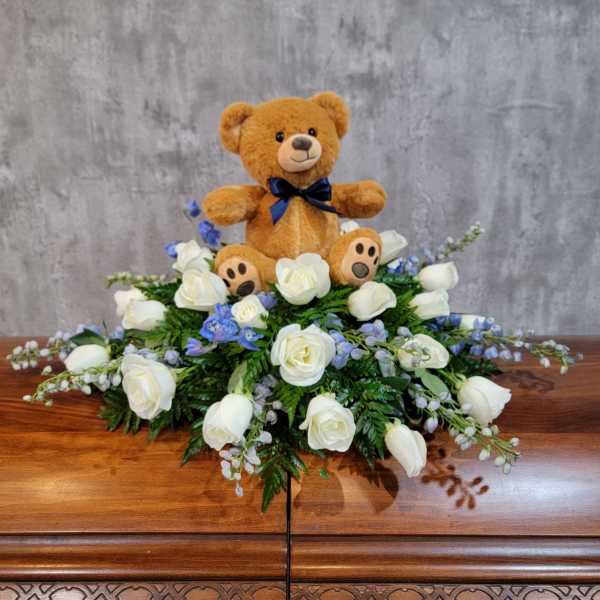 Teddy bear sitting in a white rose arrangement with blue flowers