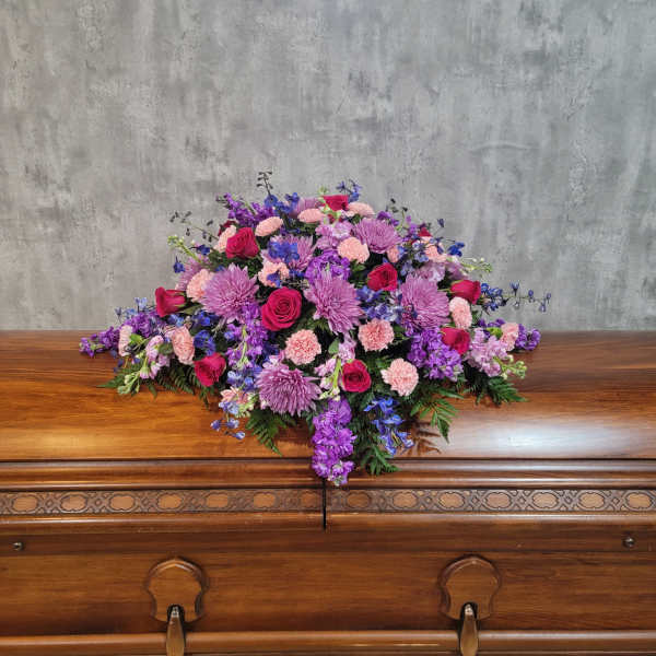 Large pink, purple, and blue floral spray on a wooden casket