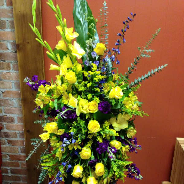 Tall floral arrangement with yellow roses and purple flowers in a black stand
