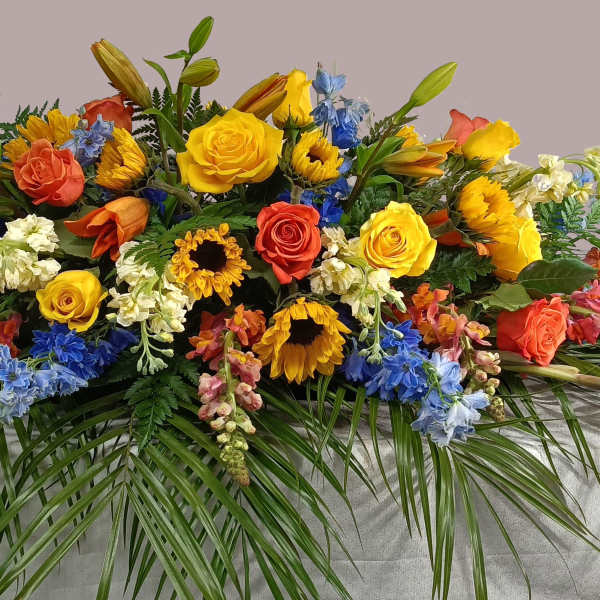 Large casket spray with yellow, orange, blue, and white flowers