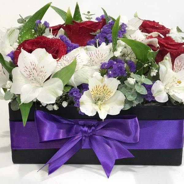 Red and white flowers arranged in a black box with a purple ribbon