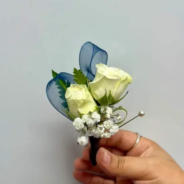 White rose boutonniere with blue ribbon loops and baby's breath