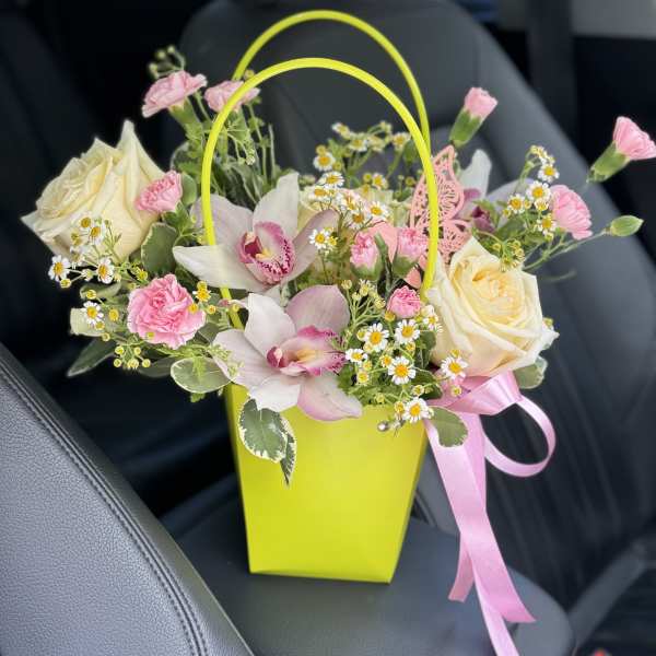 Pink and cream flowers in a bright yellow gift bag with a pink ribbon