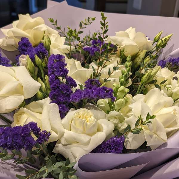 Bouquet of white roses and purple filler flowers wrapped in lavender paper