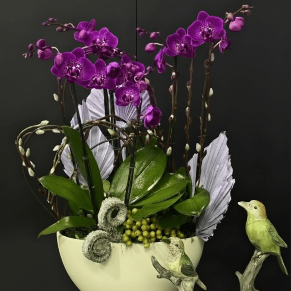 Purple orchids arranged in a white bowl with decorative bird figurines