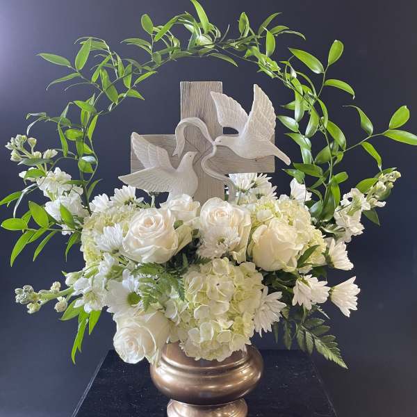 White floral arrangement with roses, hydrangeas, and a cross topper