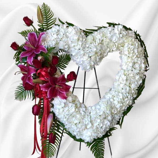 Heart-shaped white floral wreath with pink lilies and red roses on an easel
