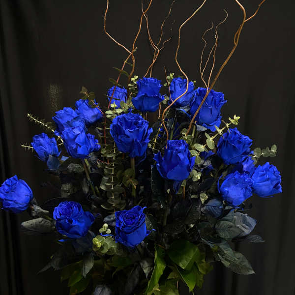 Arrangement of vivid blue roses in a tall vase with curly branches