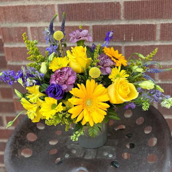 Yellow and purple mixed flower arrangement in a gray vase