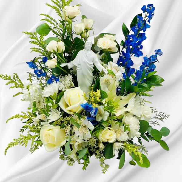White roses and blue flowers arranged around a white statue