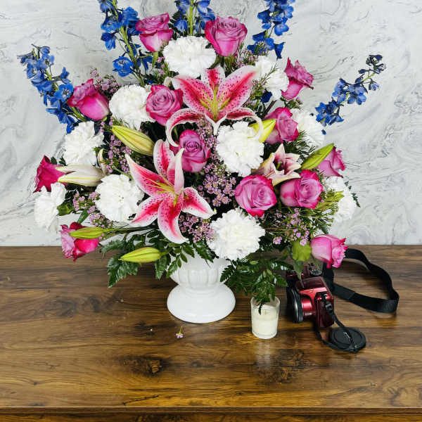 Pink roses and lilies in a white vase with blue delphinium and white carnations